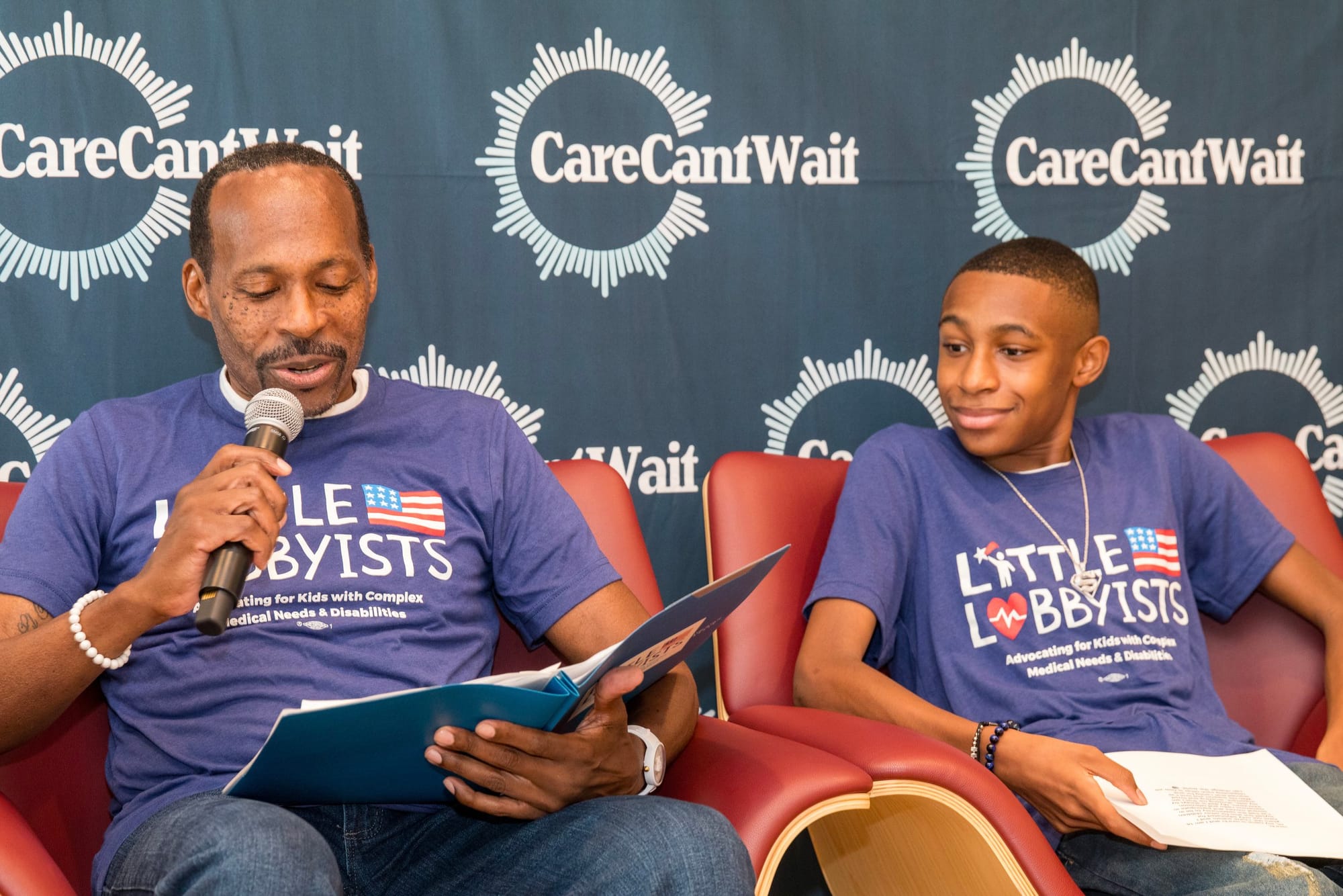 Rico & Isra'El Winston speak at the summit. A Care Can't Wait backdrop is behind them, and they are seated, wearing primary blue Little Lobbyists t-shirts. Photo credit: Tirrea Billings