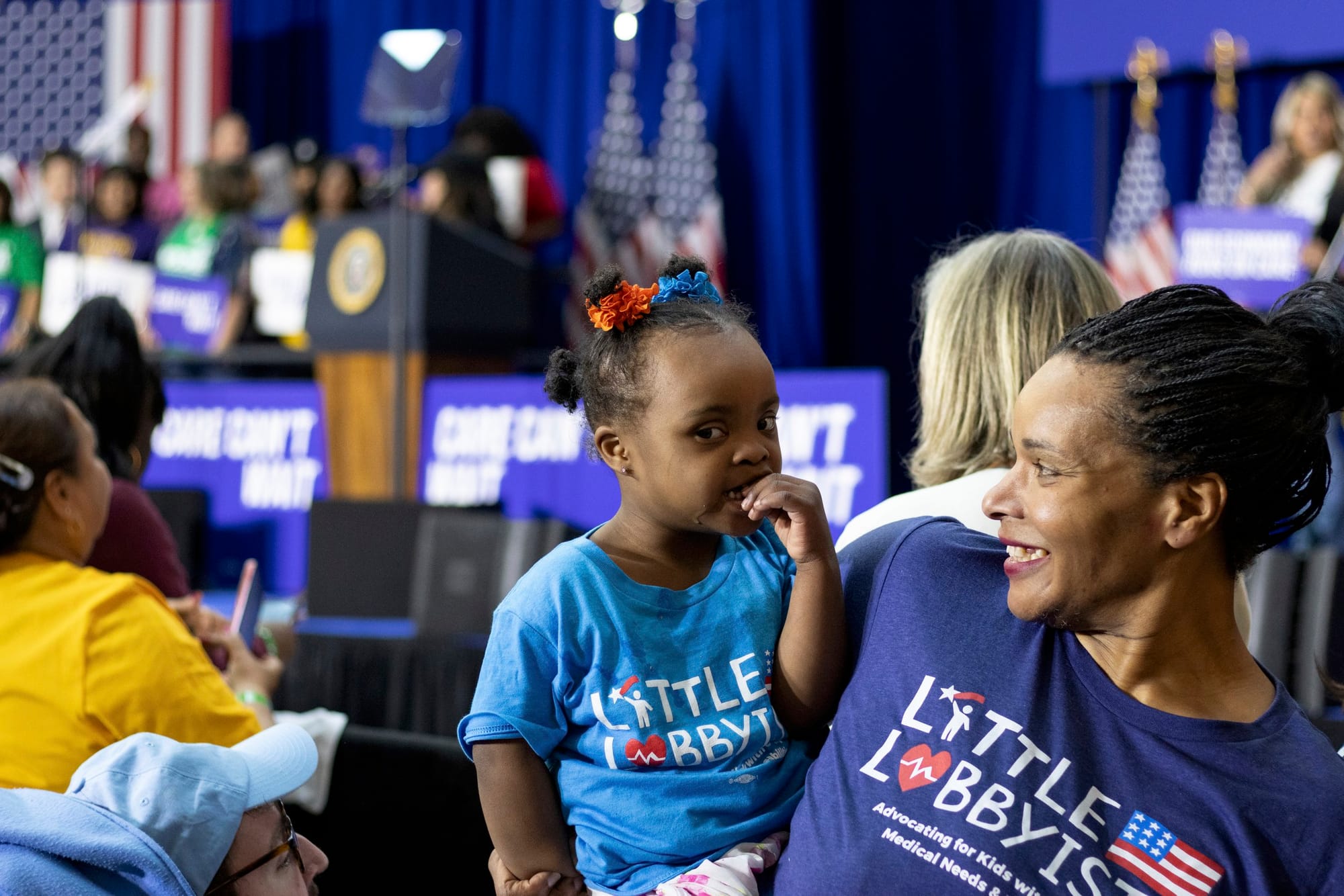 Danielle, who has elaborate cornrows and is wearing her Little Lobbyists royal blue shirt (as are all our members), holds her toddler daughter Destiny. They are looking at each other and smiling.
