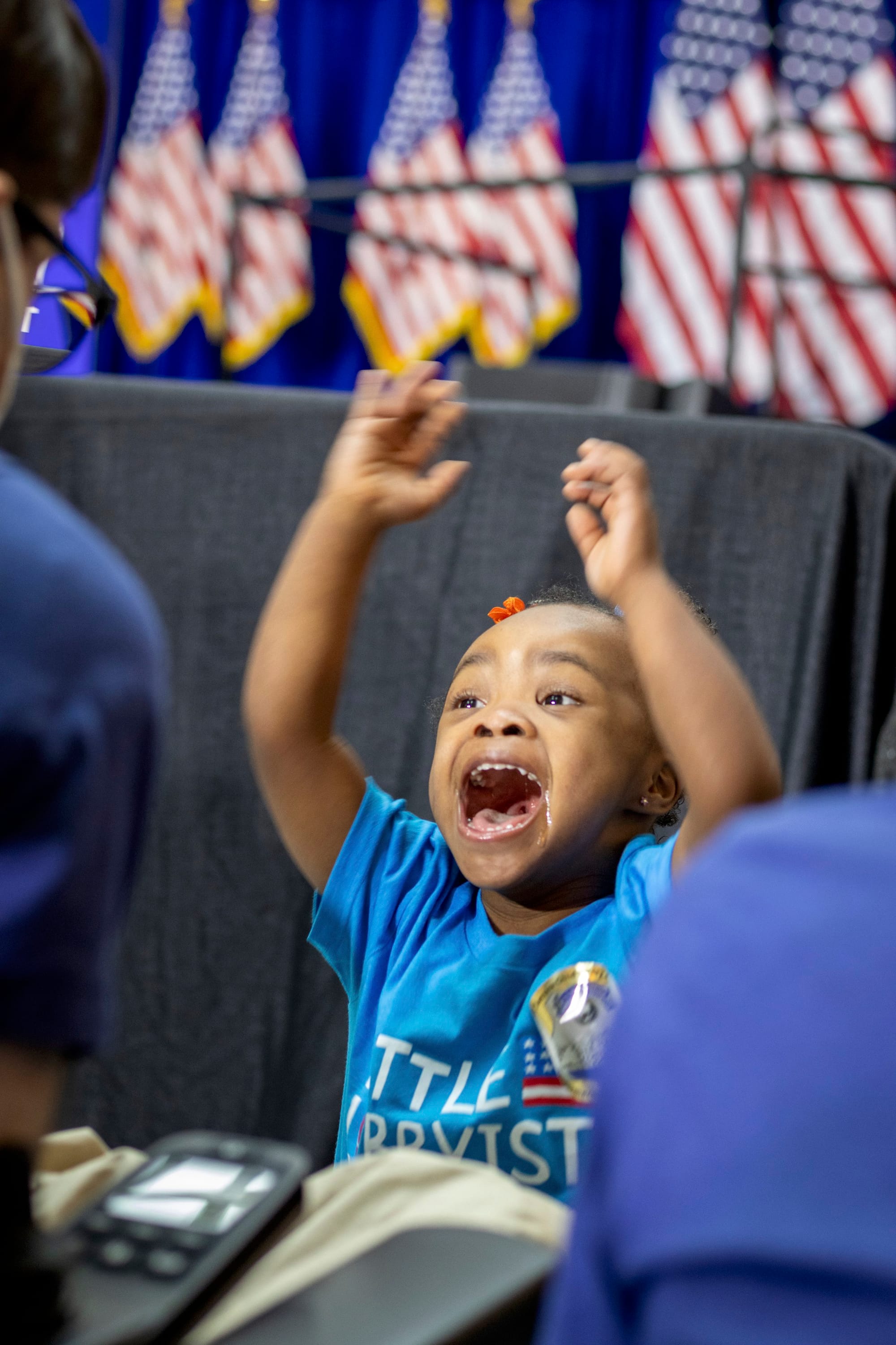 Destiny raises her arms high in joy. Behind her is the stage with a row of American flags.