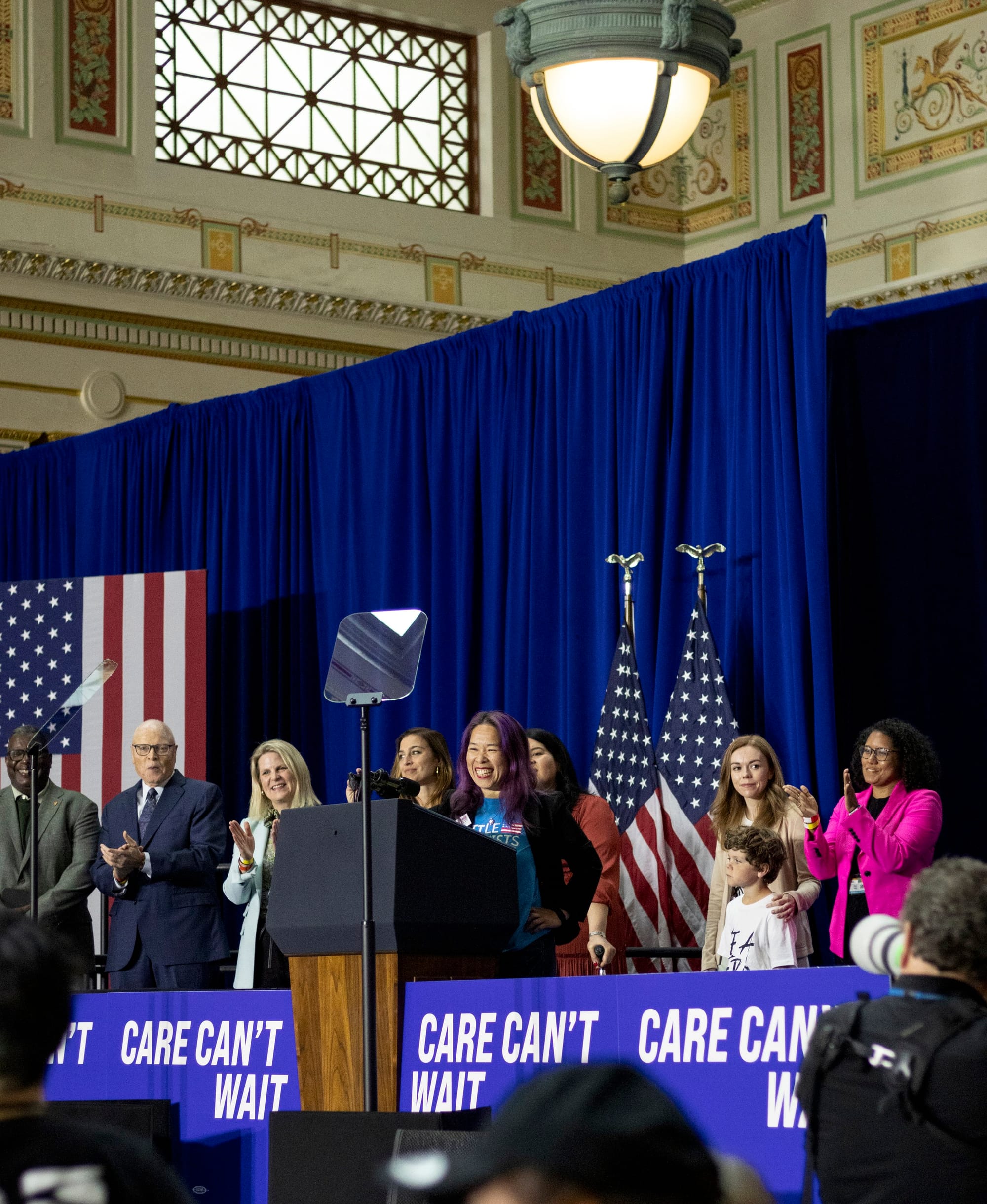 Elena speaks from the stage at the rally. To each side of her are other speakers.