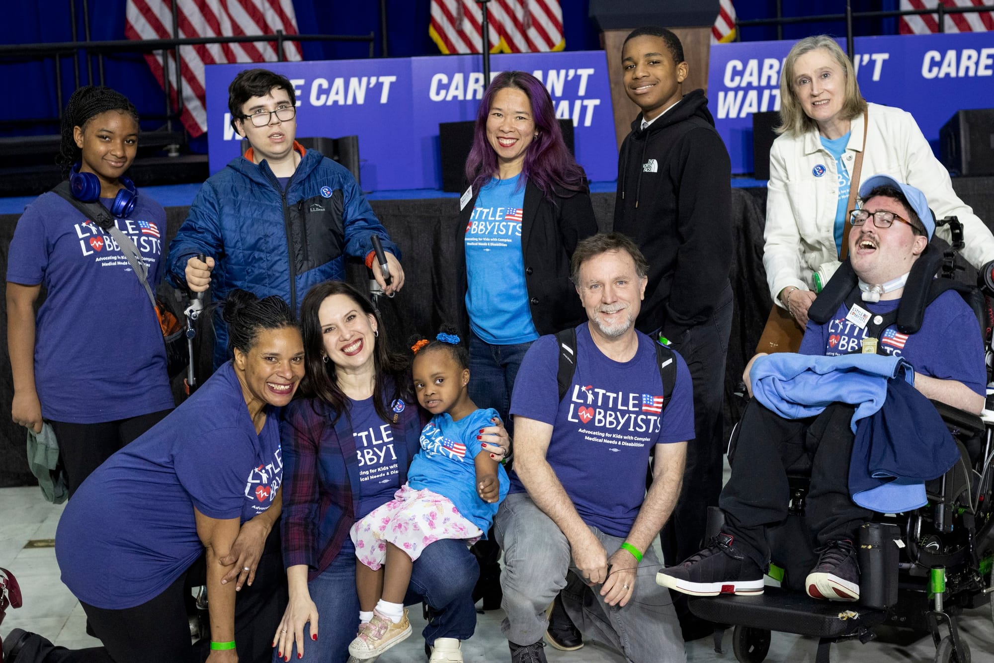 A group of us pose in front of the stage—some are using mobility devices, some are standing, some are kneeling on the floor.