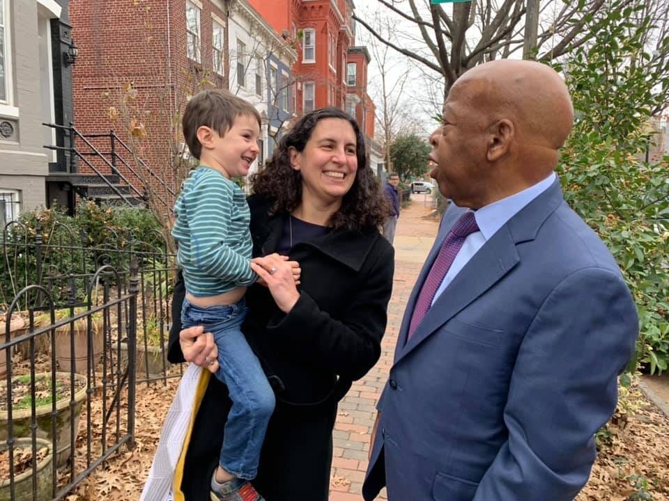 A mom holding a young boy in her arms speaks to a well-known member of the U.S. House of Representatives on a brick-covered city street in Washington, D.C.