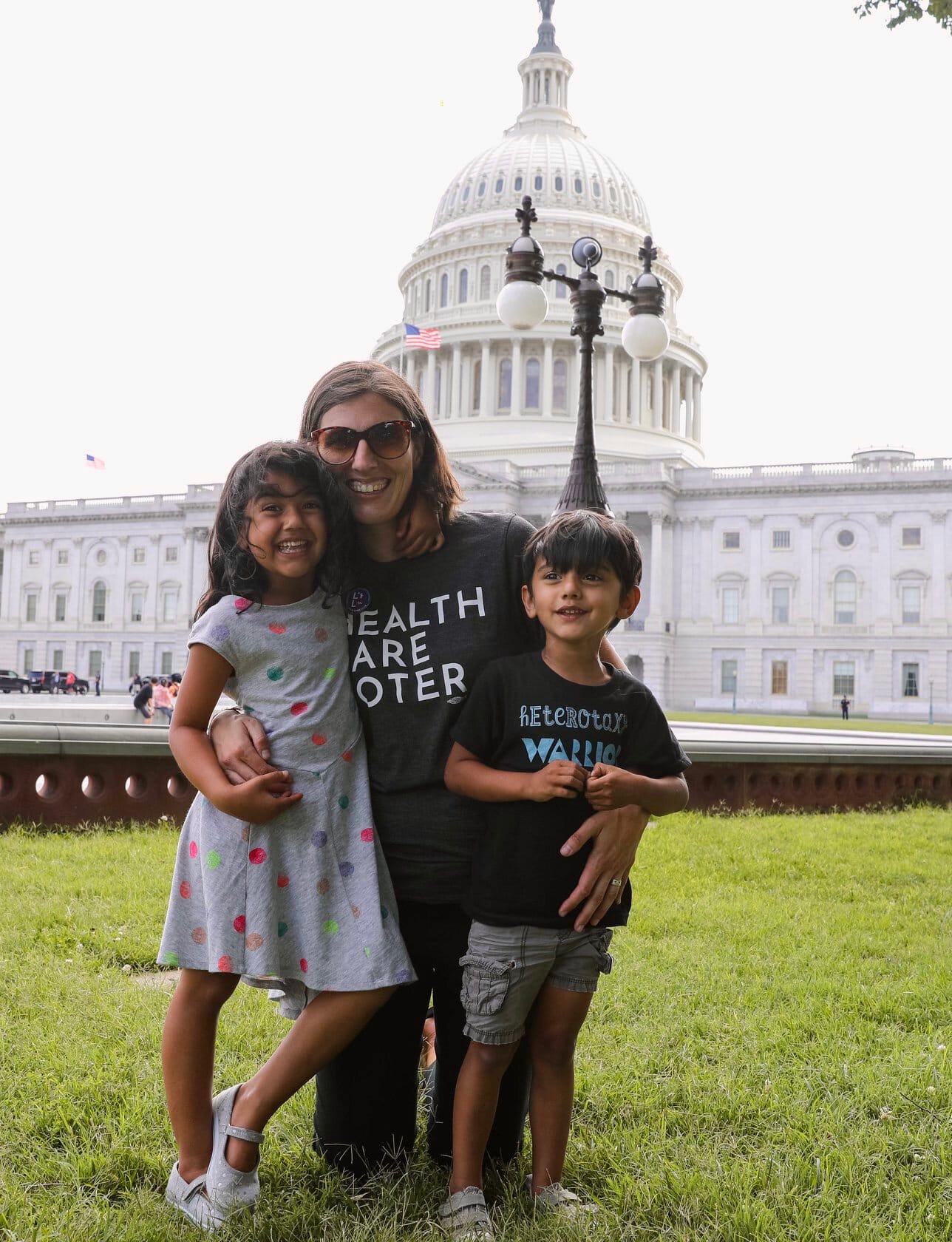 A mom wearing a “Health Care Voter” t-shirt poses in front of the U.S. Capitol while hugging her children.