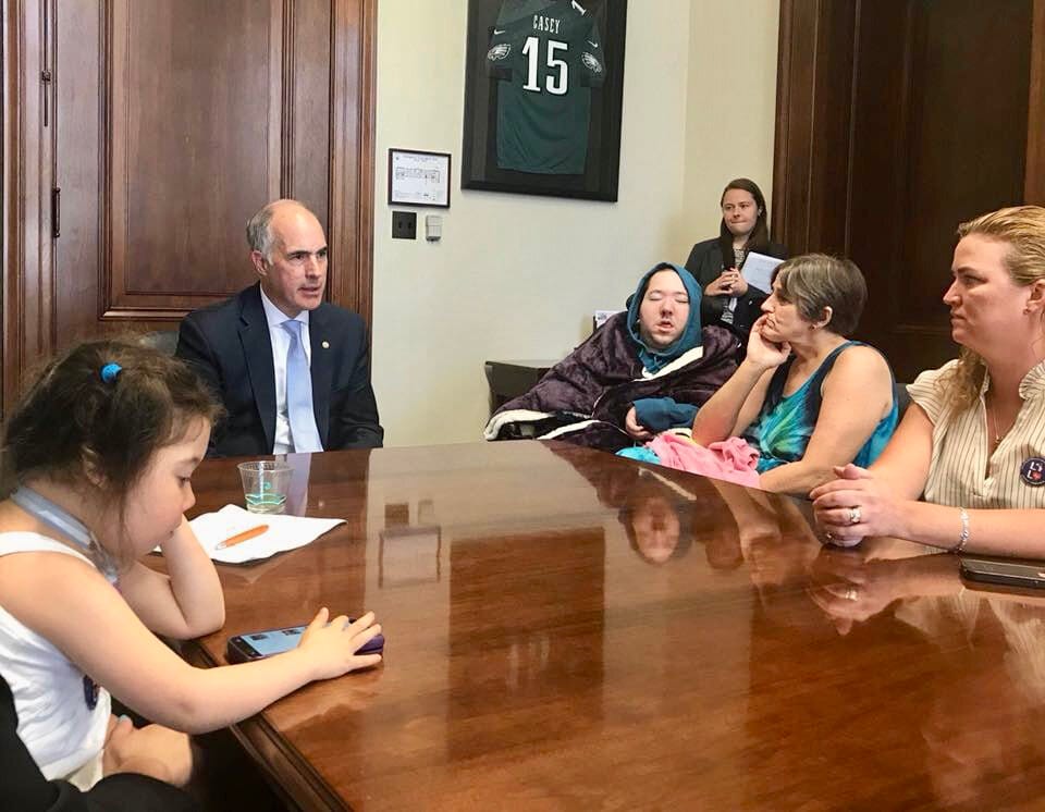 Children and parents are seated around a large wooden conference table in a congressional office.