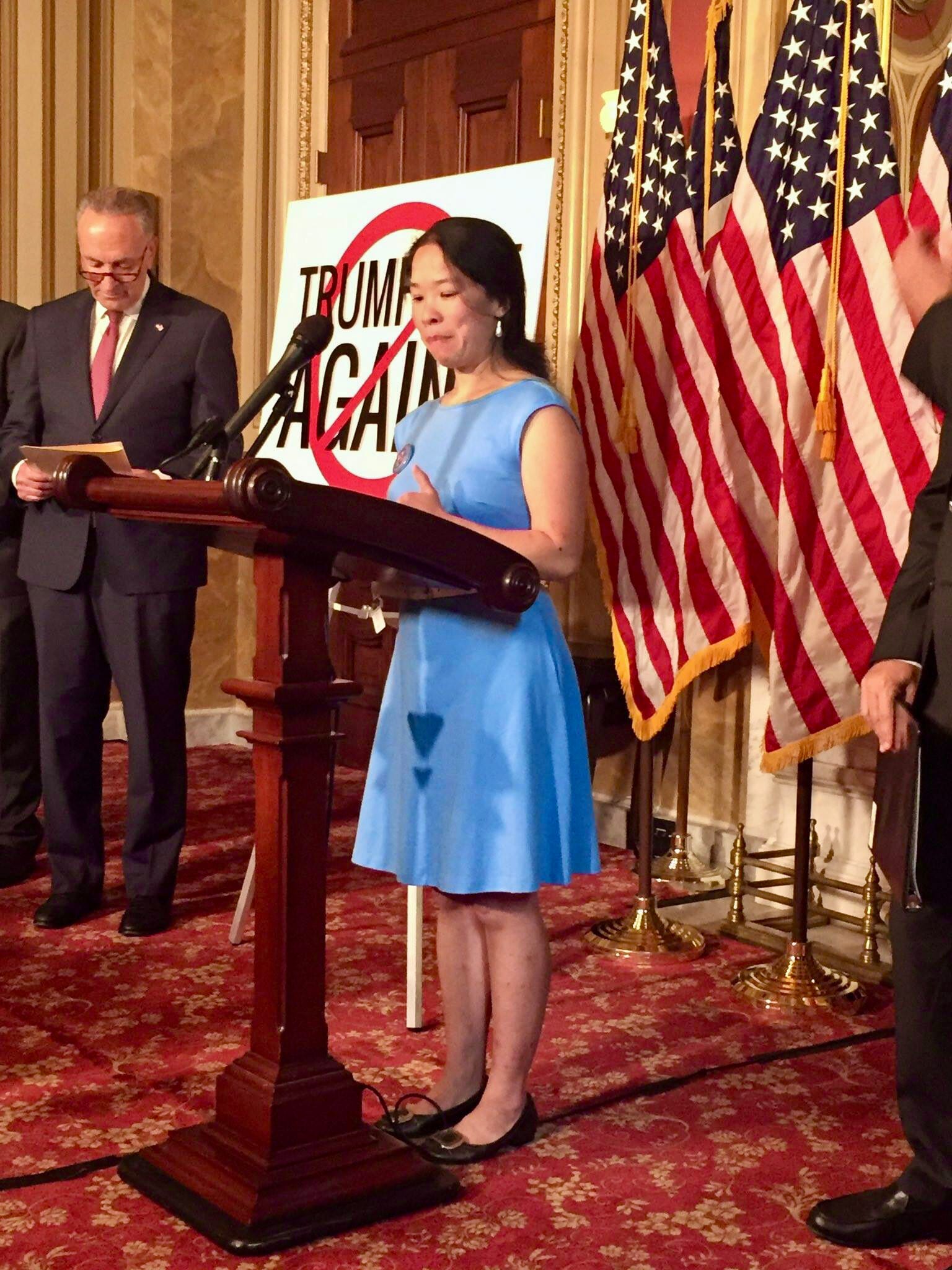 A founder of Little Lobbyists delivers remarks from a podium in the Capitol building. Flags are in the background.