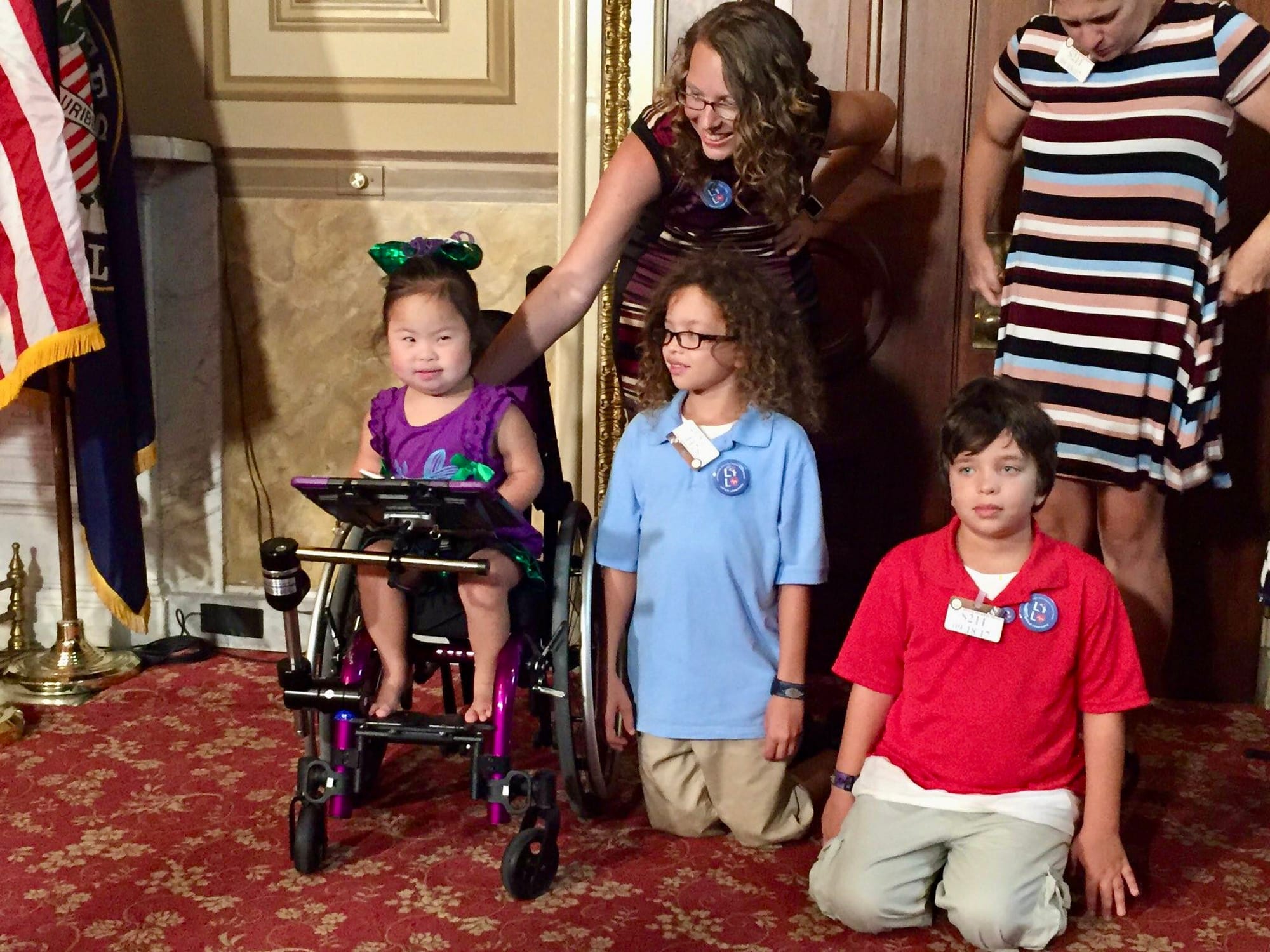 Little Lobbyists families pose during a press conference, sitting by decorative doors to the room.
