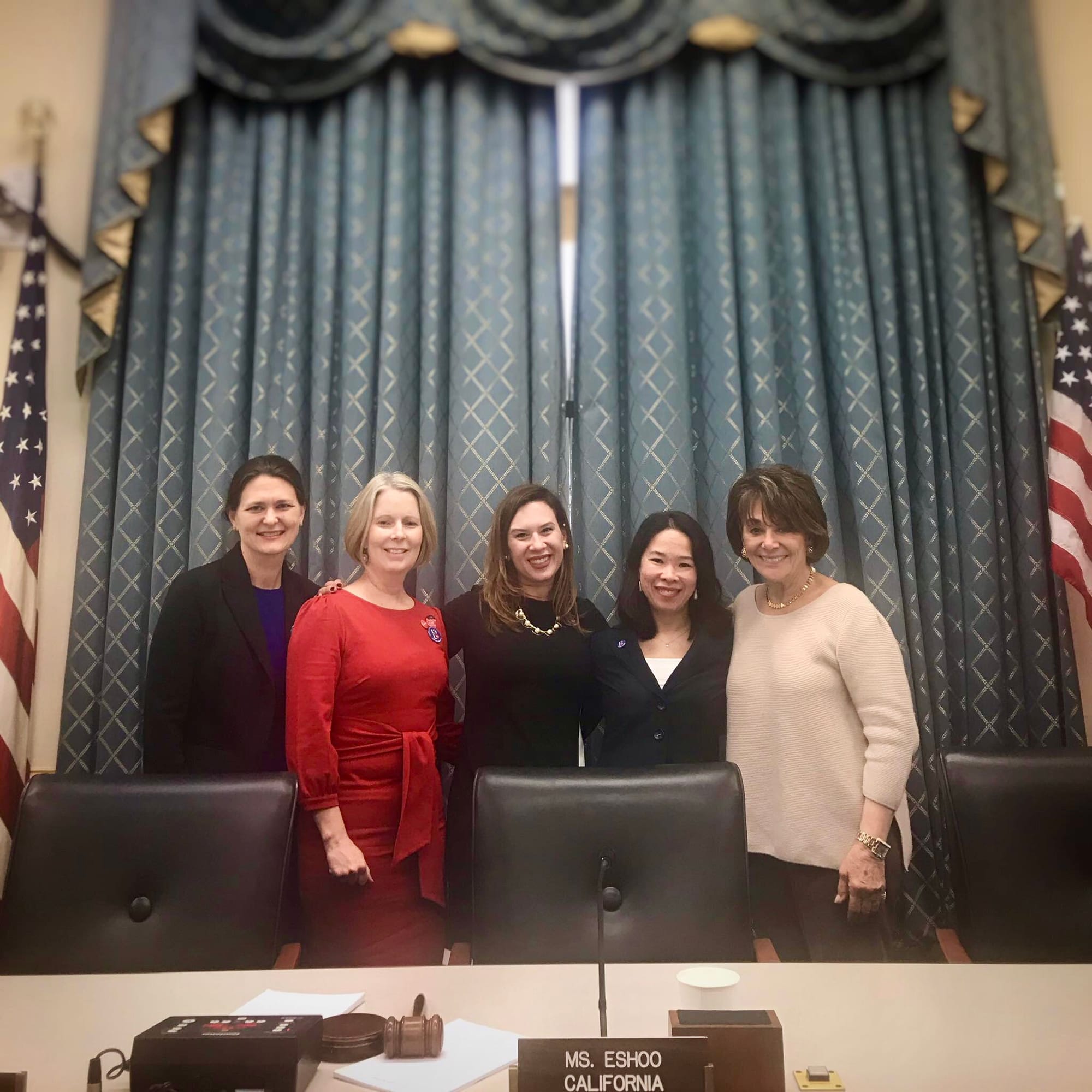 Several women pose in front of decorative curtains after making remarks about health care.