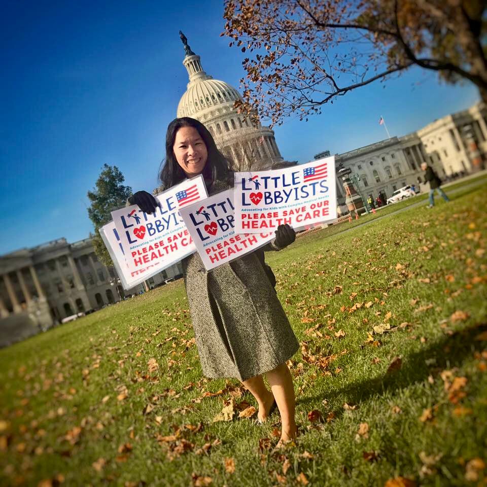 A founder of Little Lobbyists holds multiple LL signs with the LL logo in front of the U.S. Capitol on a beautiful autumn day.