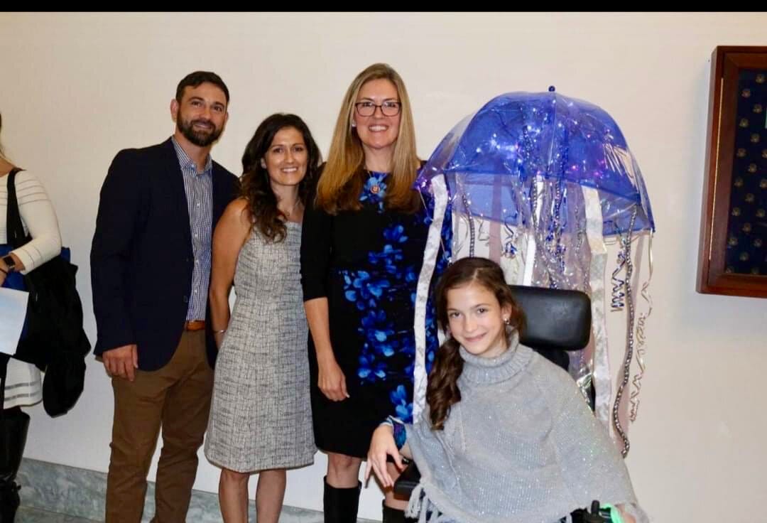 A young girl whose wheelchair has been turned into a beautiful jellyfish Halloween costume poses with her parents and a member of Congress.