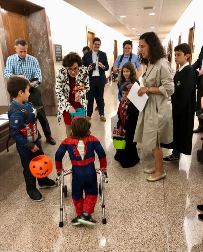 A group of Little Lobbyists in Halloween costumes speak in a hallway of a congressional office building with a legislator.