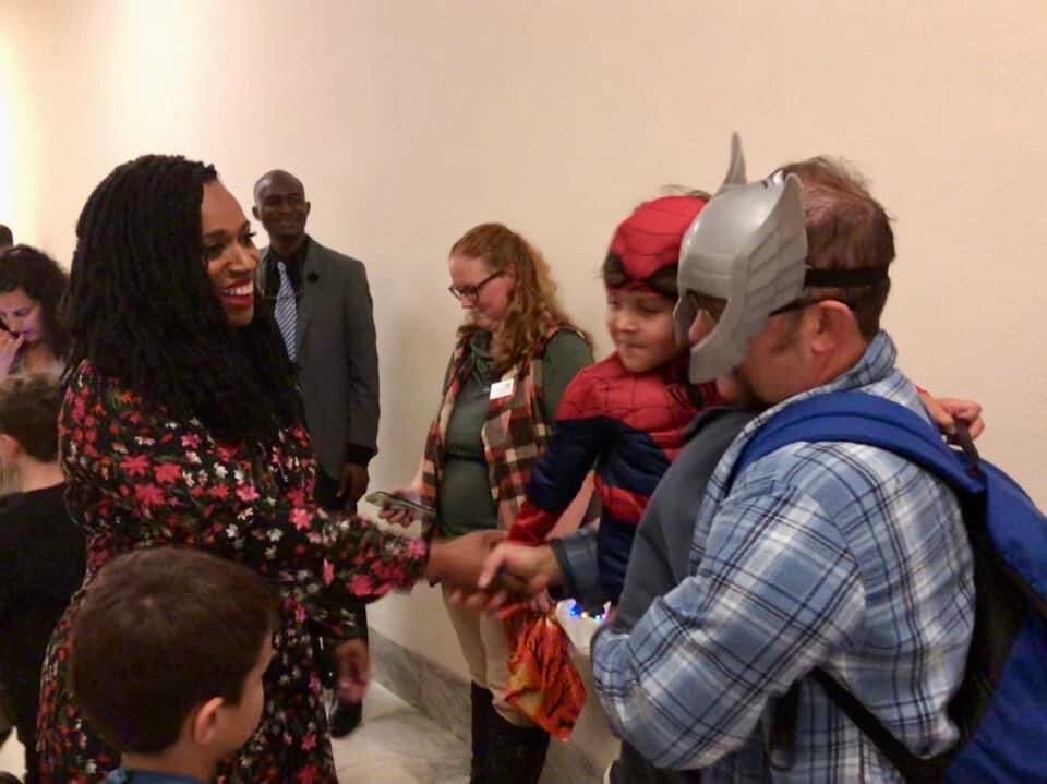 A father and son dressed as superheroes accept a Halloween treat from a member of Congress.