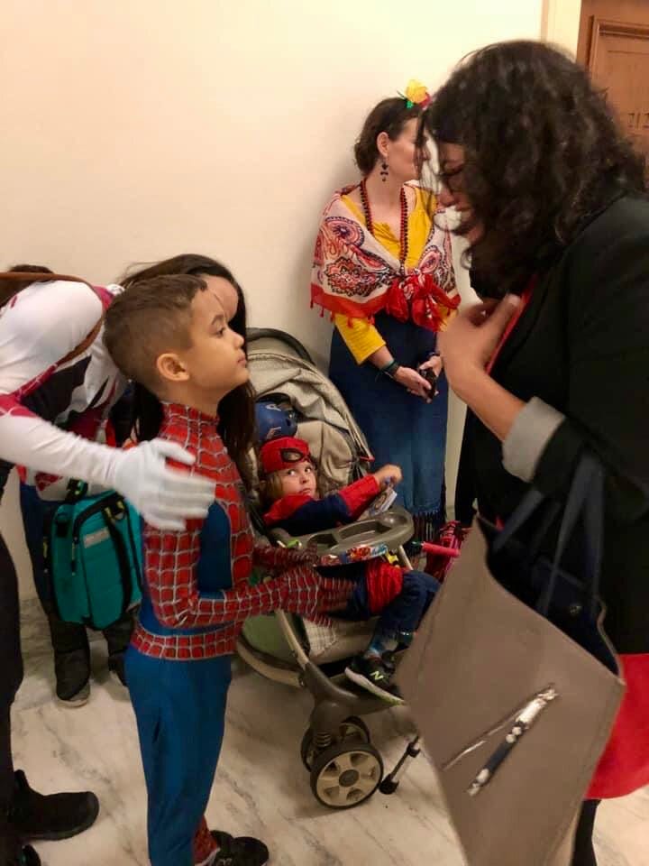 A young boy wearing a superhero costume speaks with a member of Congress in a hallway in one of the congressional office buildings.