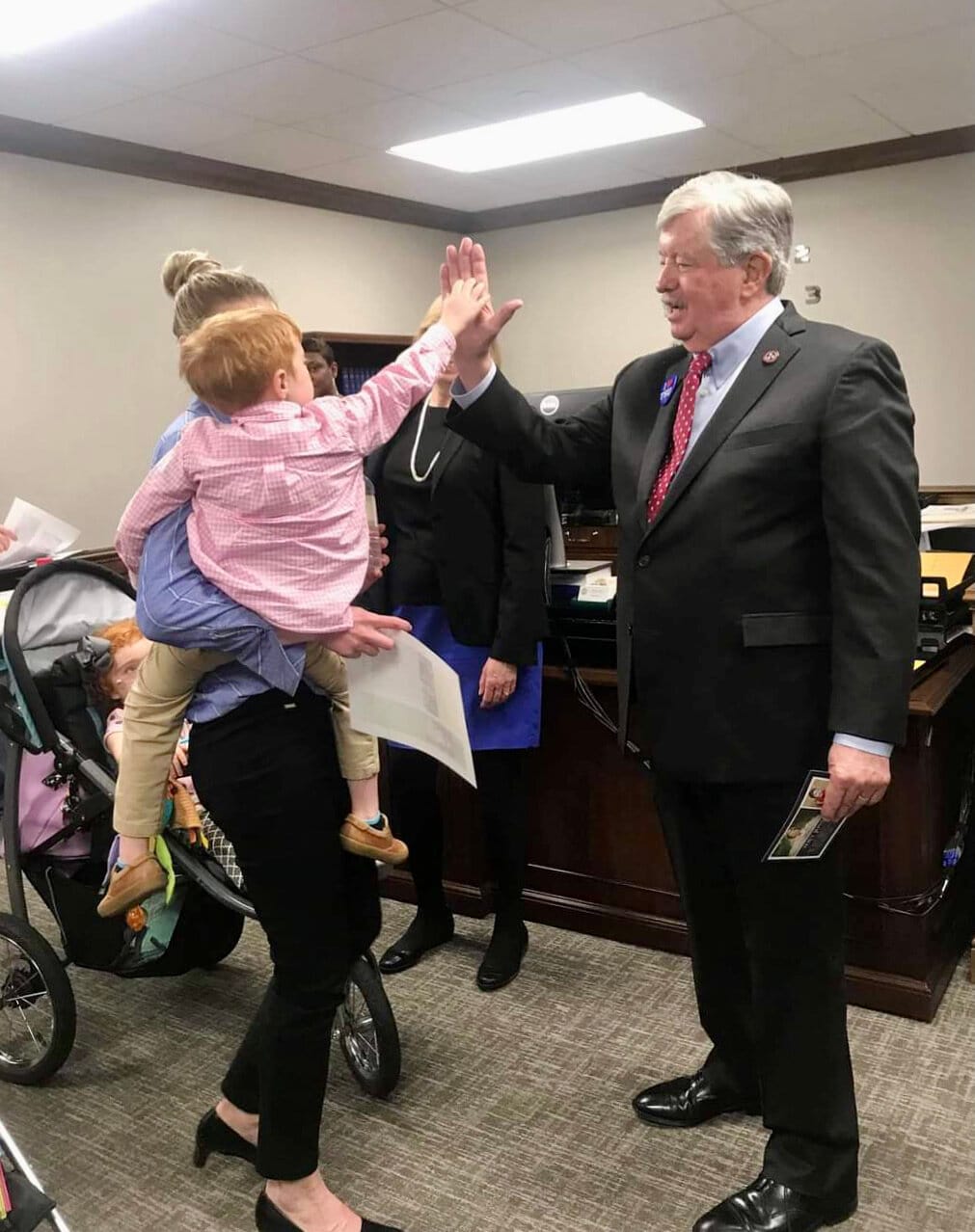 A mom holds a young girl who gives a legislator a high-five.