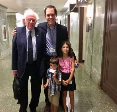 In a marble-lined hallway of a congressional office building, a dad and his kids pose with a U.S. Senator.