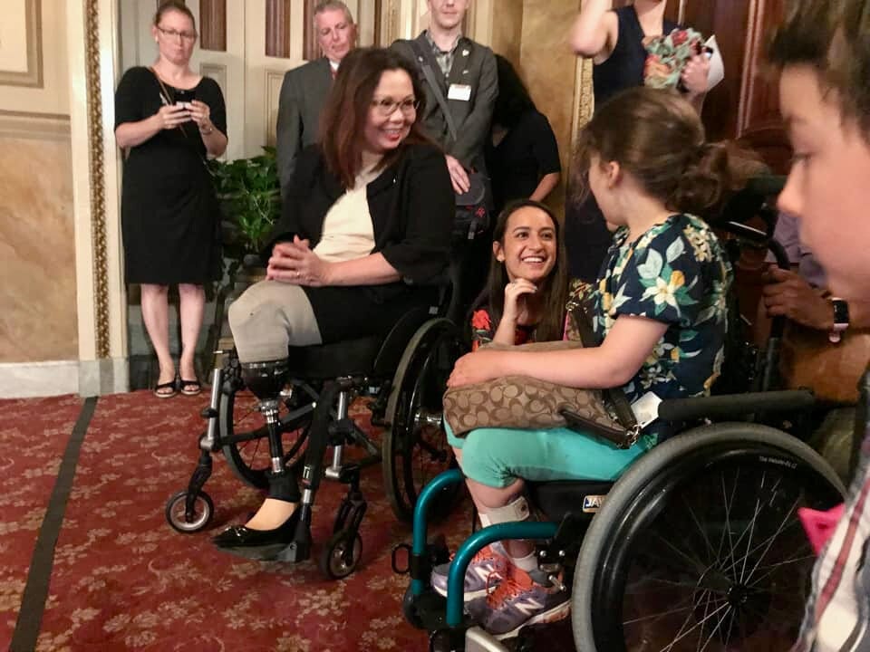 A young girl who is a wheelchair user poses with a U.S. Senator who is also a wheelchair user.