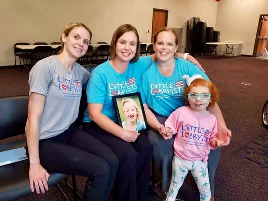 Mallorie, at left, poses with other members of Little Lobbyists Tennessee chapter. From left to right, Mallorie, Jessica Fox, Michelle Gross, and Asher. The group spoke at a town hall for Stop the Block. [image description: Three moms wearing grey a…