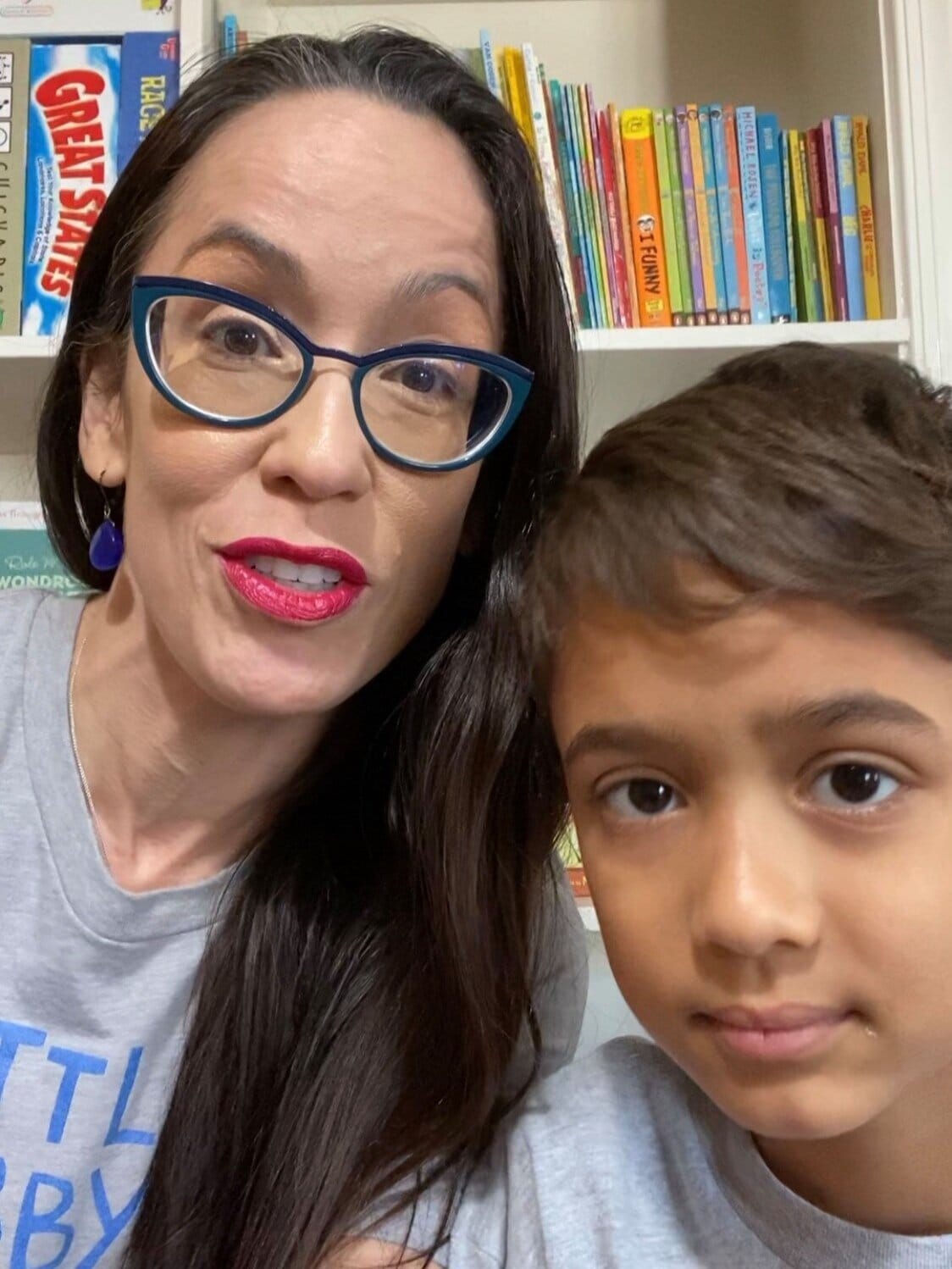 Walewska and her son Aire. [image description: A mother &amp; son pose in front of a bookcase. The mom has long black hair &amp; wears blue-frame glasses. The son has short dark hair.]Walewska y su hijo Aire. [descripción de la imagen: Una madre e h…