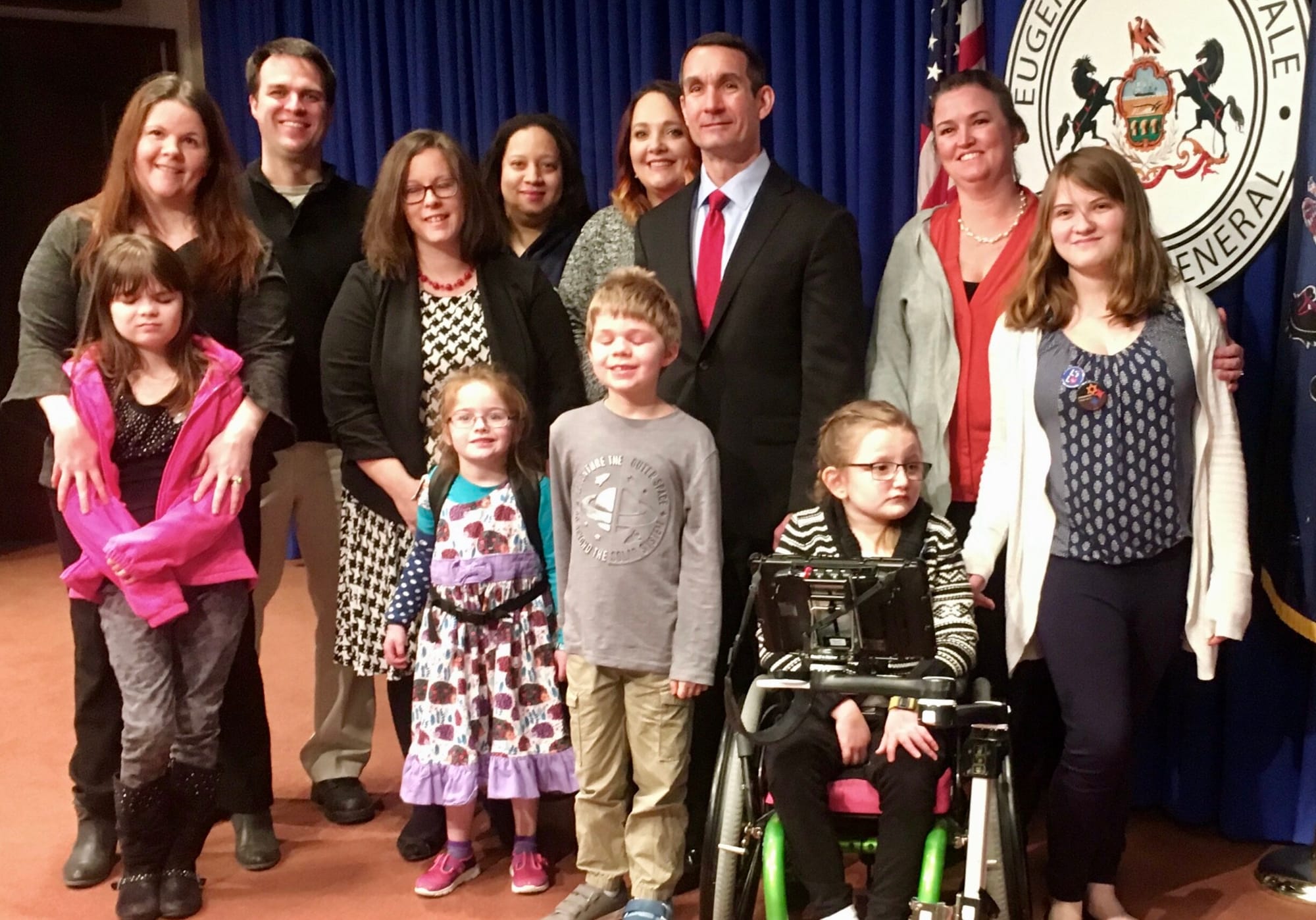 Eugene DePasquale (center) standing in front of a blue curtain with a group of Little Lobbyists Pennsylvania families.
