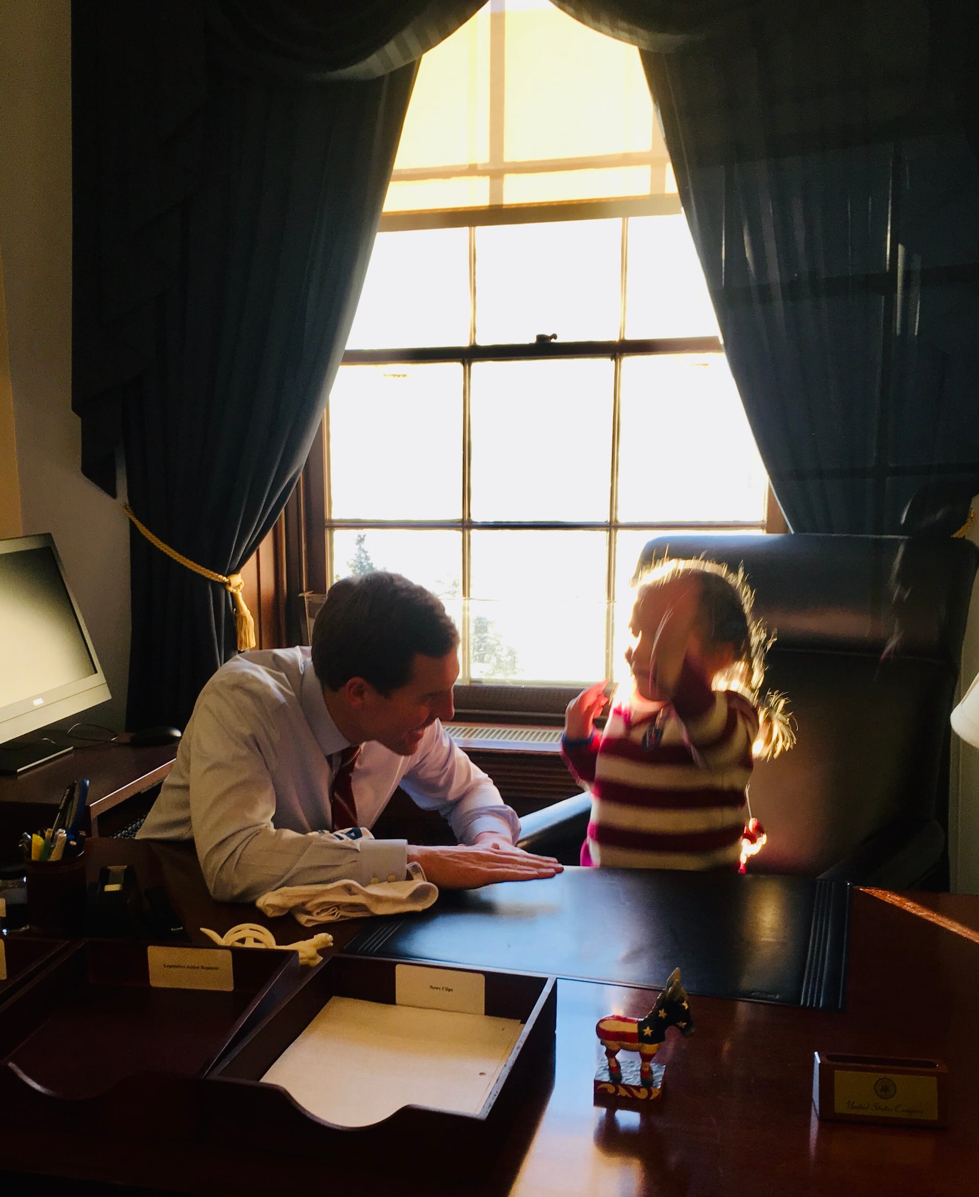 Conor Lamb drumming on his desk in Washington DC with Abby seated in his chair drumming excitedly along with him. Both are smiling broadly.