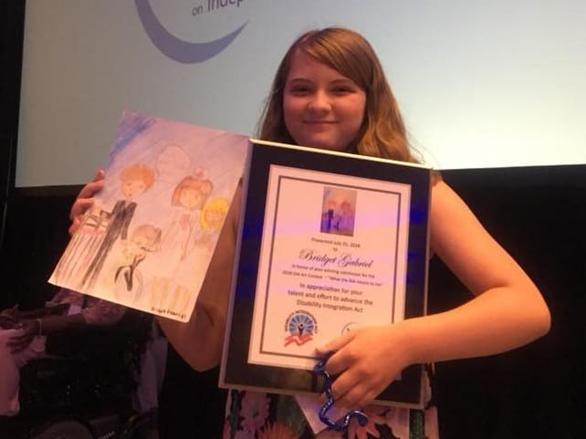 Image Description: Abby’s sister Bridget with her award from NCIL and her award-winning artwork about “What the DIA Means to Me.”