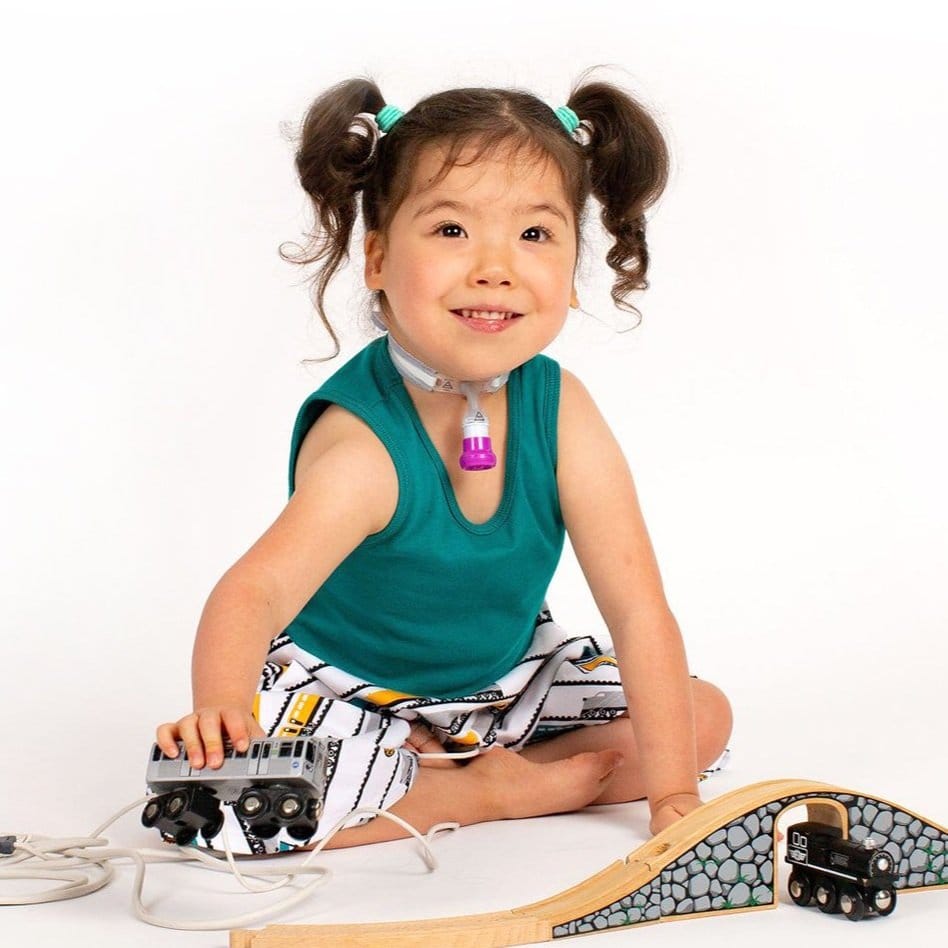 photo of Xiomara, an Asian girl with pigtails and a tracheostomy playing with wooden trains and smiling