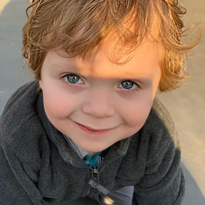 Cole a little boy with blond curls and blue eyes smiling up at the camera