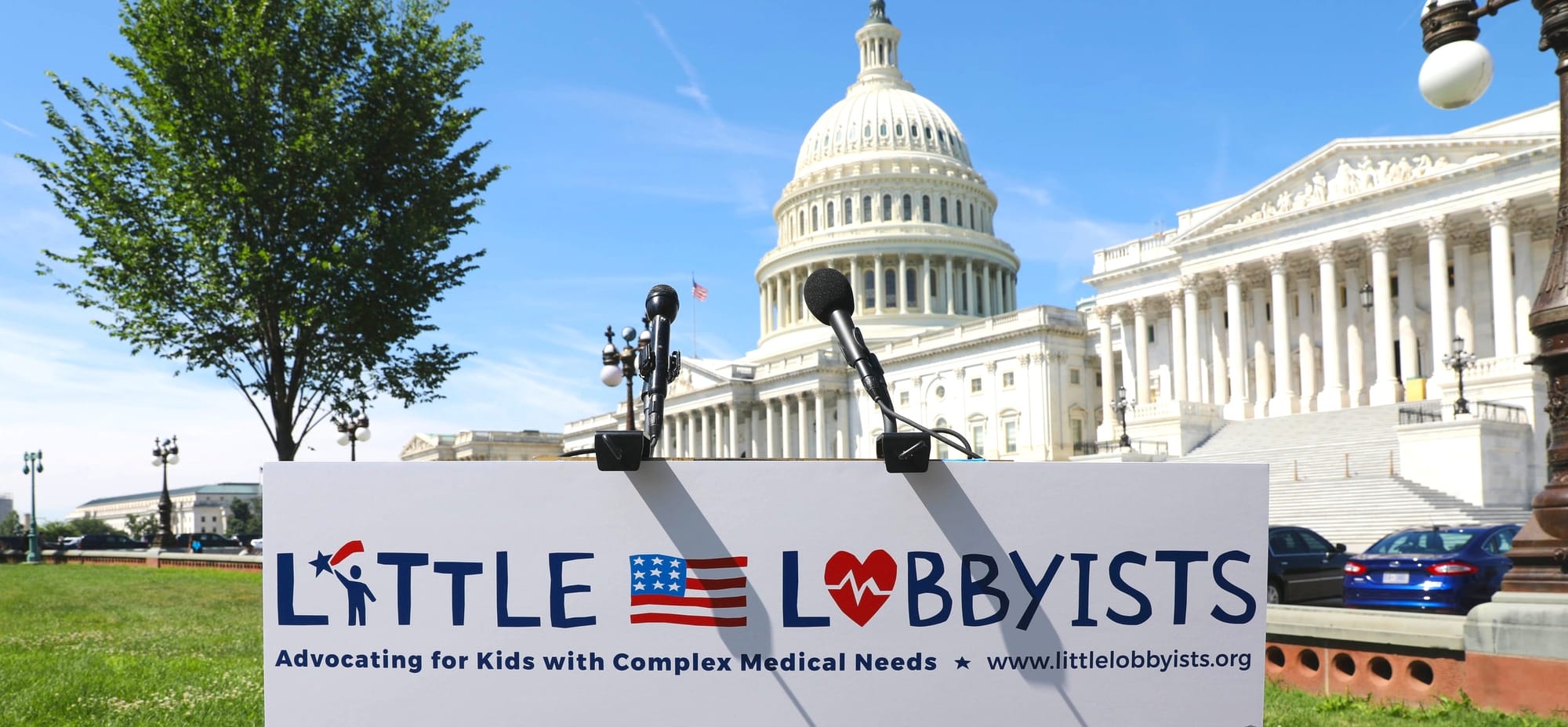 Podium with a Little Lobbyists sign and mic in front of the Capitol on a clear summer day.