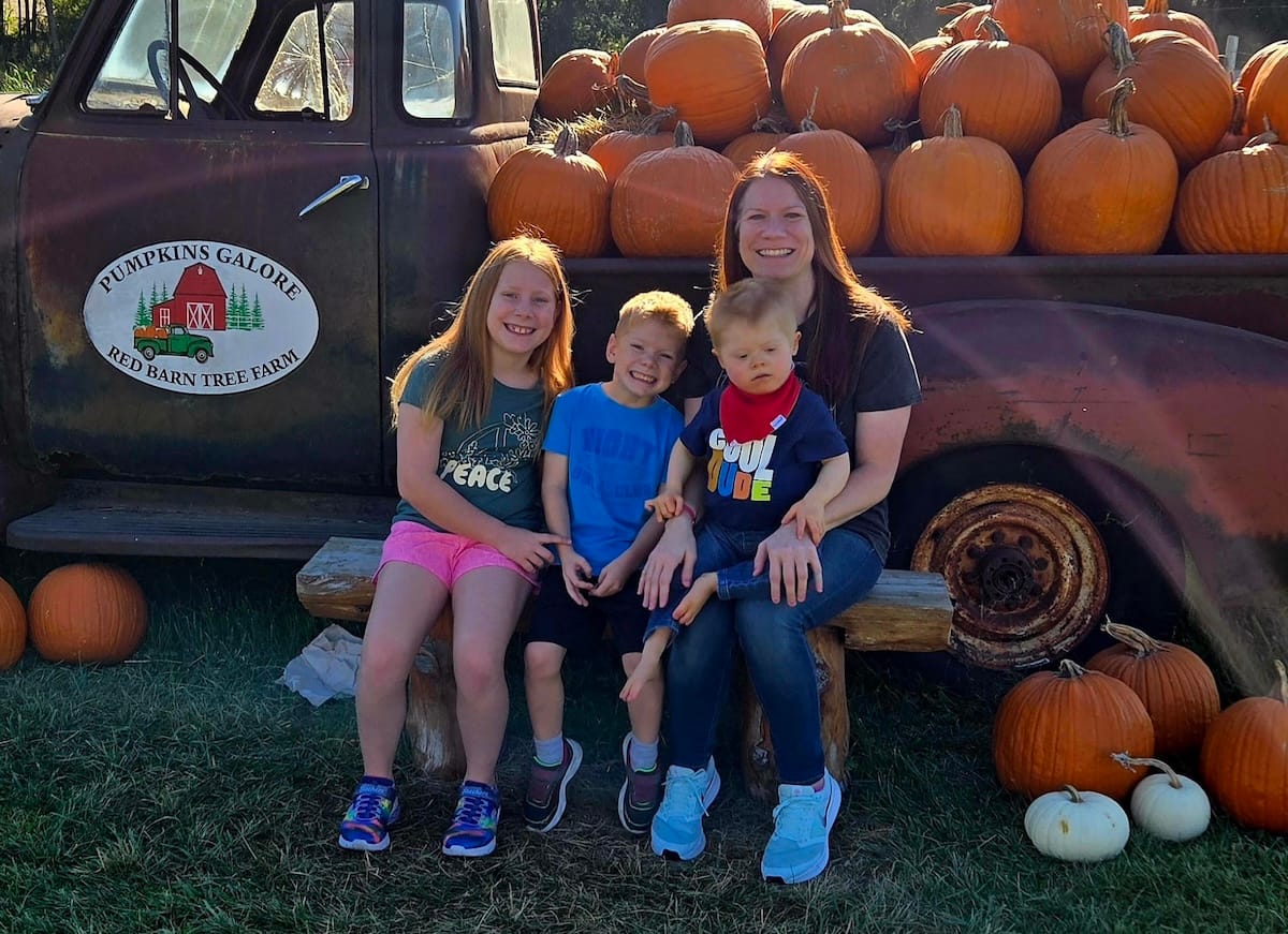 Teresa, Charla, Anthony, and Alex at a fall festival. They're sitting on the fender of a vintage truck covered in pumpkins.